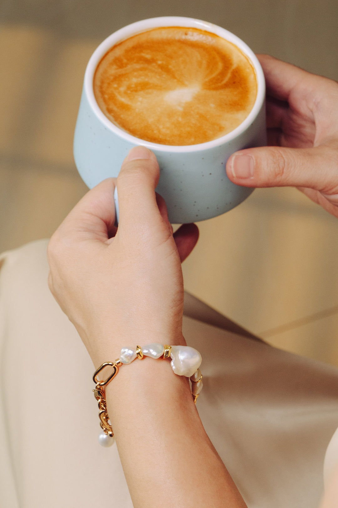 A modal is holding a cup of coffee with a gold filled bracelet with two large baroque pearls and four small keshi pearls. There is a teardrop pearl attached to the end of the extender. The clasp is a lobster clasp.