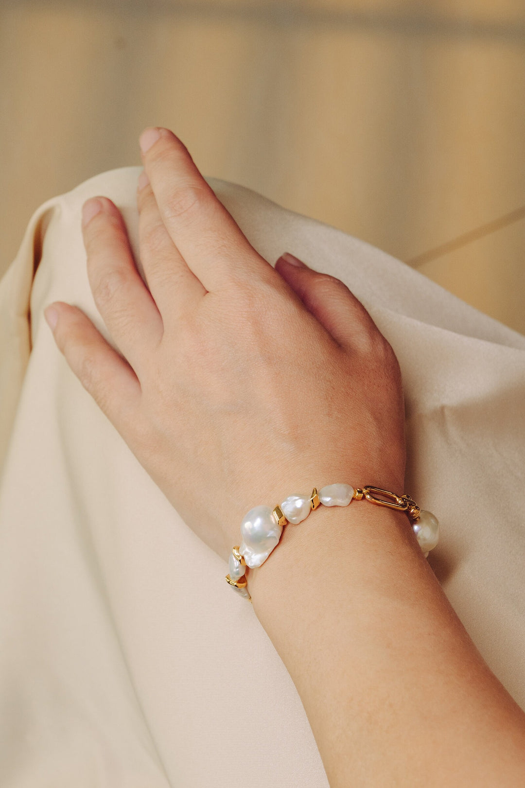 a modal is wearing a gold filled bracelet with two large baroque pearls and four small keshi pearls. There is a teardrop pearl attached to the end of the extender. The clasp is a lobster clasp.