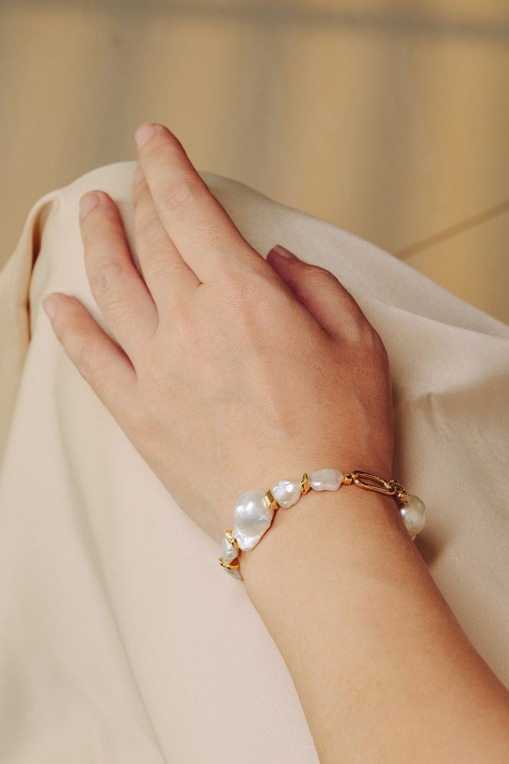 a modal is wearing a gold filled bracelet with two large baroque pearls and four small keshi pearls. There is a teardrop pearl attached to the end of the extender. The clasp is a lobster clasp.