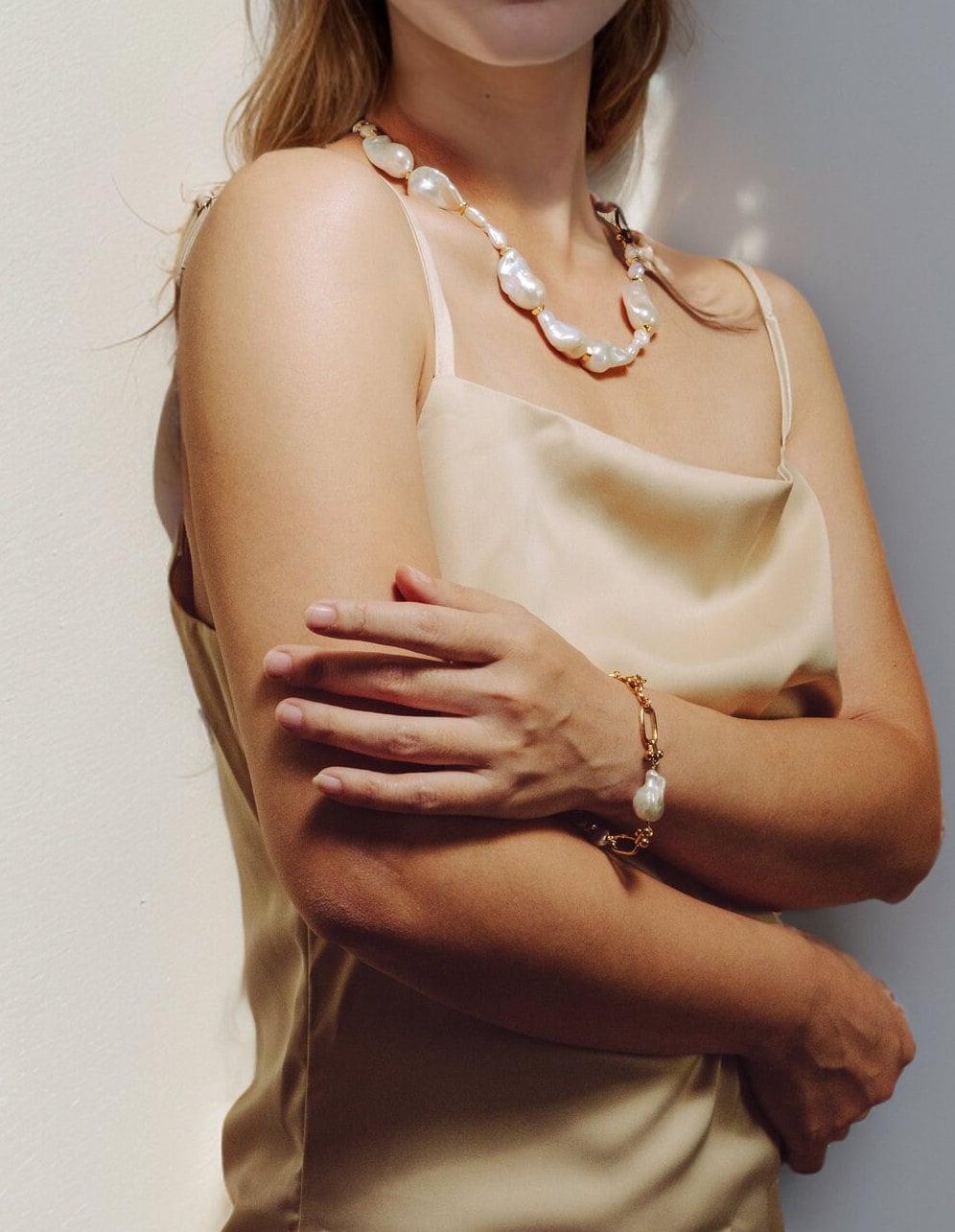 A modal is wearing a set of pearl jewelry with a gold filled bracelet and a necklace. The bracelet has two large baroque pearls and four small keshi pearls. There is a teardrop pearl attached to the end of the extender. The clasp is a lobster clasp.